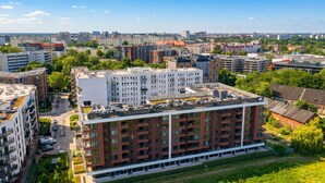Un edificio de varios pisos con techo plano, rodeado de vegetación y otros edificios.