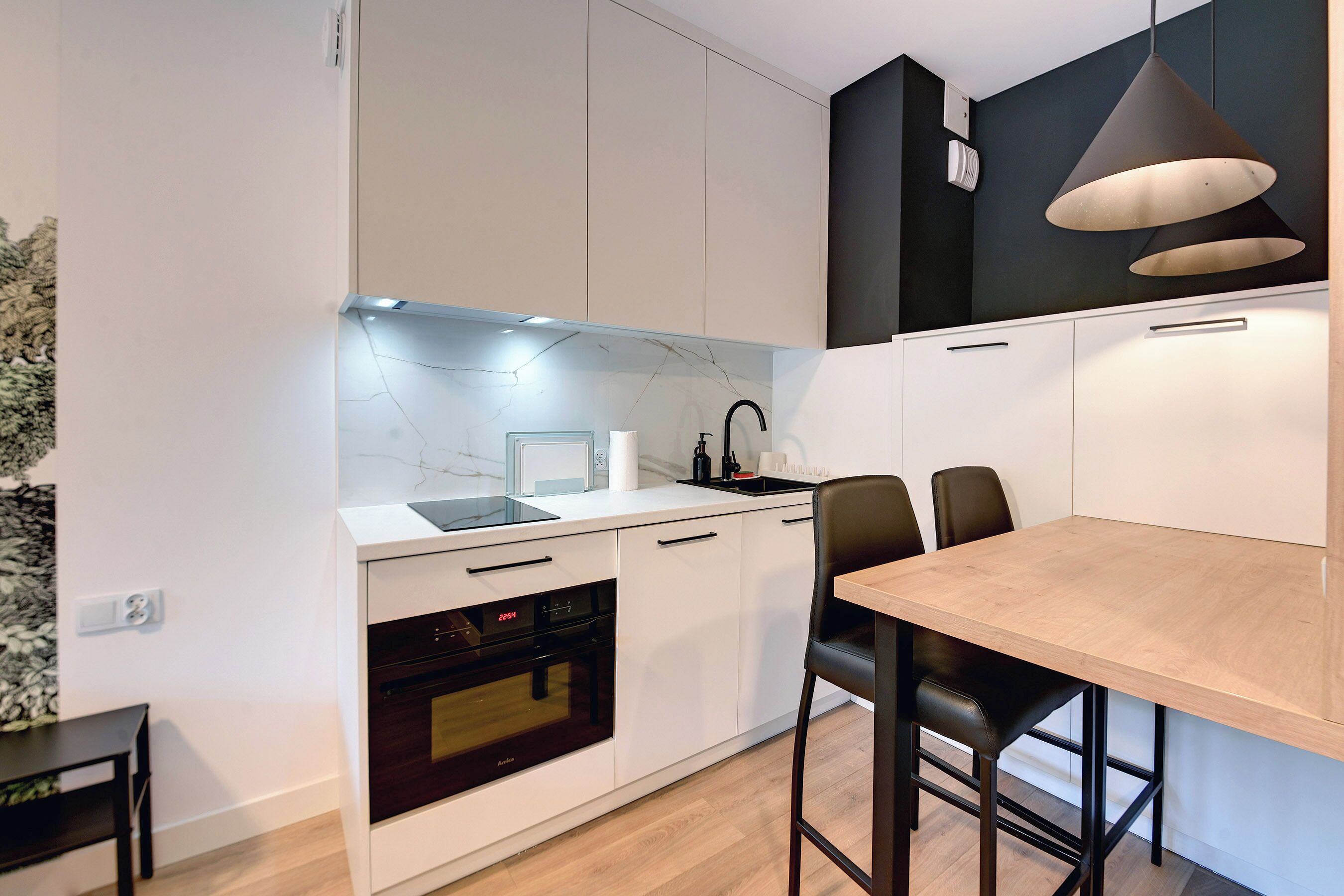 Une cuisine moderne avec des armoires blanches, un four encastré, un évier et un coin repas comprenant une table et des chaises.