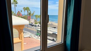 A room with a large window overlooking a beach, palm trees, and a road with vehicles. - Terrace with Sea Views at Castillo Bil Bil, Benalmádena (Benalmádena)