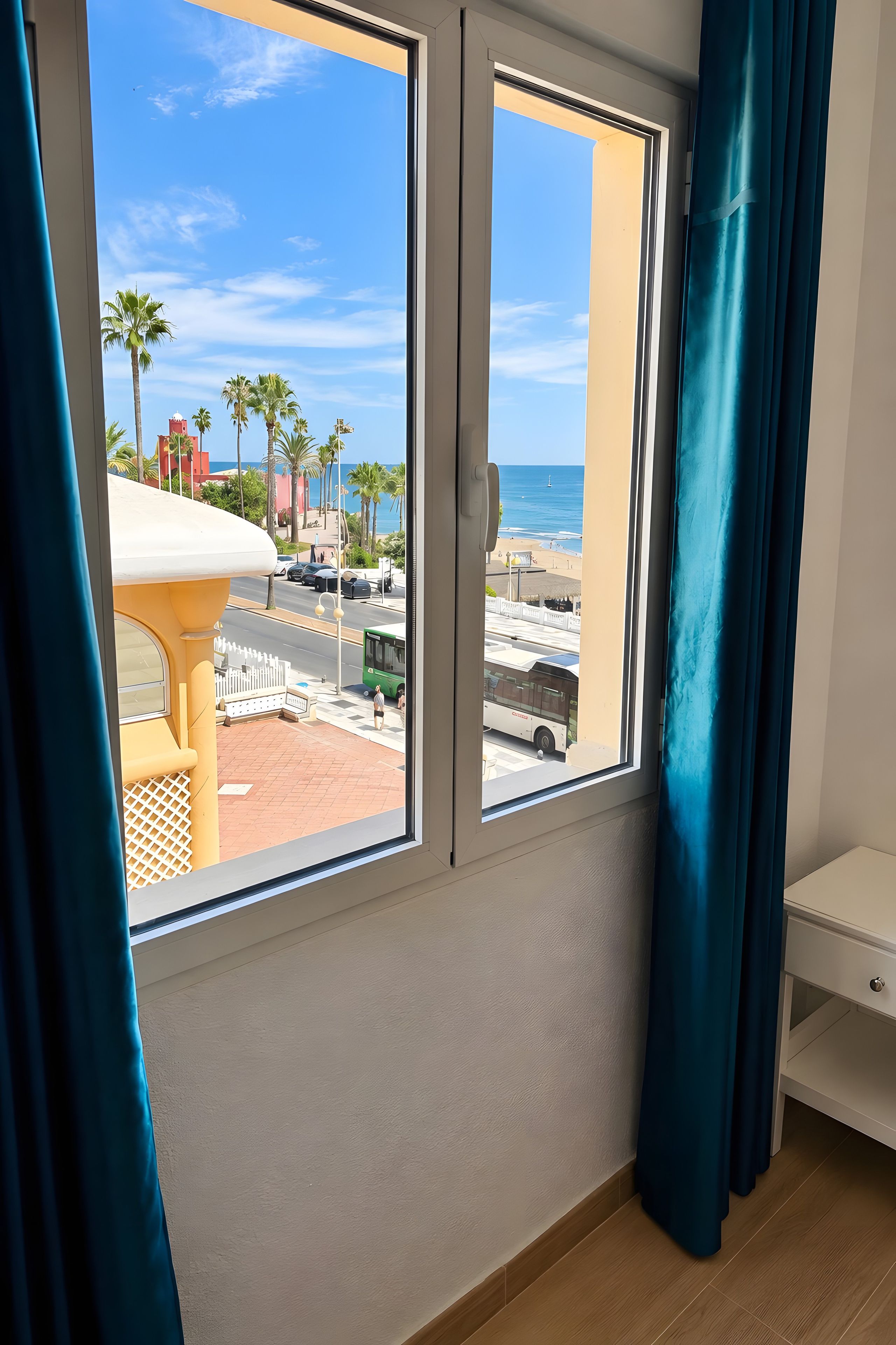 Una habitación con un ventanal grande que da a una playa, una pared blanca y un piso de madera.