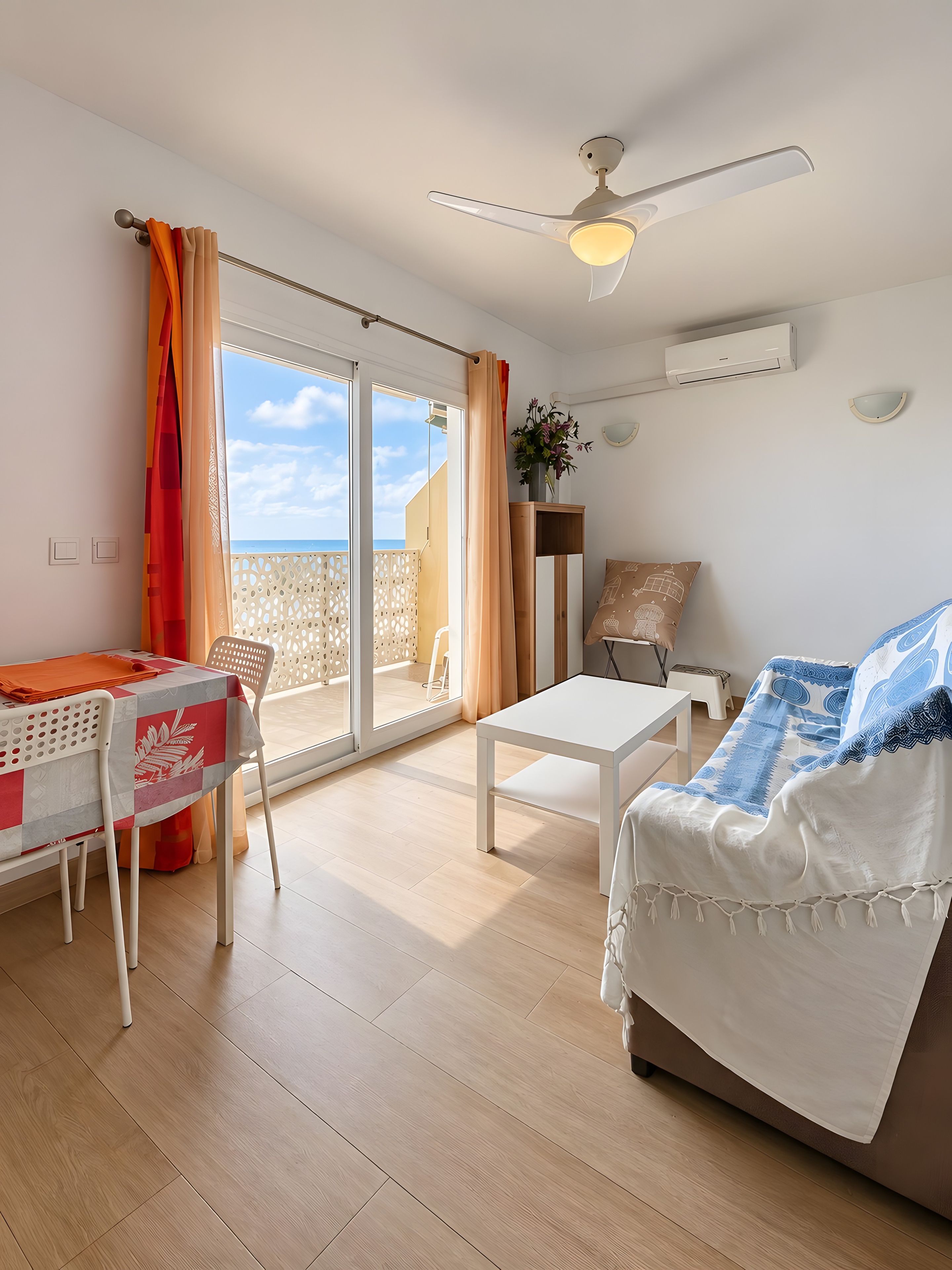 A room with a bed, a table, and a chair. There is a ceiling fan and an air conditioning unit.