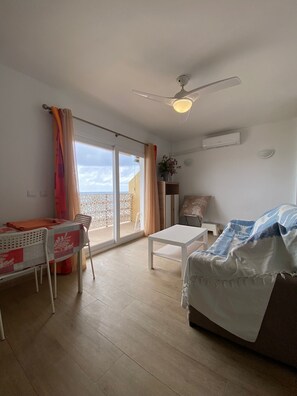 Ein Zimmer mit Bett, Tisch, Stuhl, Deckenventilator und Blick durch eine Glastür.
