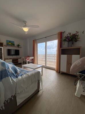 Een kamer met een bed, een bureau, een televisie, een stoel, een tafel en een balkon met uitzicht.