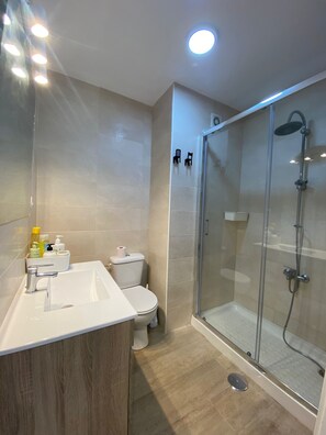 Een moderne badkamer met een douchecabine van glas, een wit wastafelmeubel met toiletartikelen en een toilet.