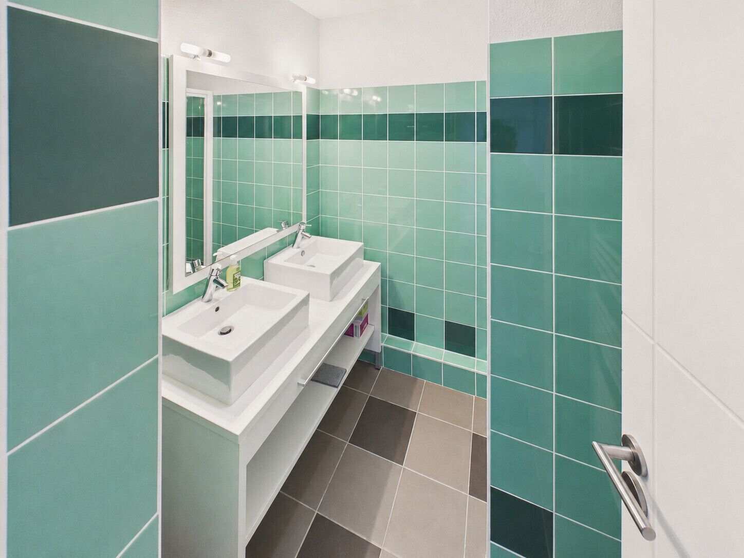 Un bagno con due lavandini, uno specchio e pareti piastrellate in verde.