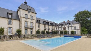 A large building with a swimming pool, multiple windows, and a fenced area with lounge chairs. - Apartment in a castle with pool – 4 guests (Baden)