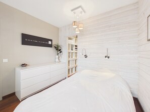 Ein Schlafzimmer mit einem Bett, einer weißen Kommode, einem Wandregal und einer Pendelleuchte.