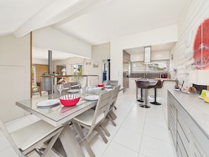 A modern kitchen with a dining area, featuring a glass table, chairs, and a red bowl. - 150m from the beach, 6-guest home with terrace (Piriac-sur-Mer)