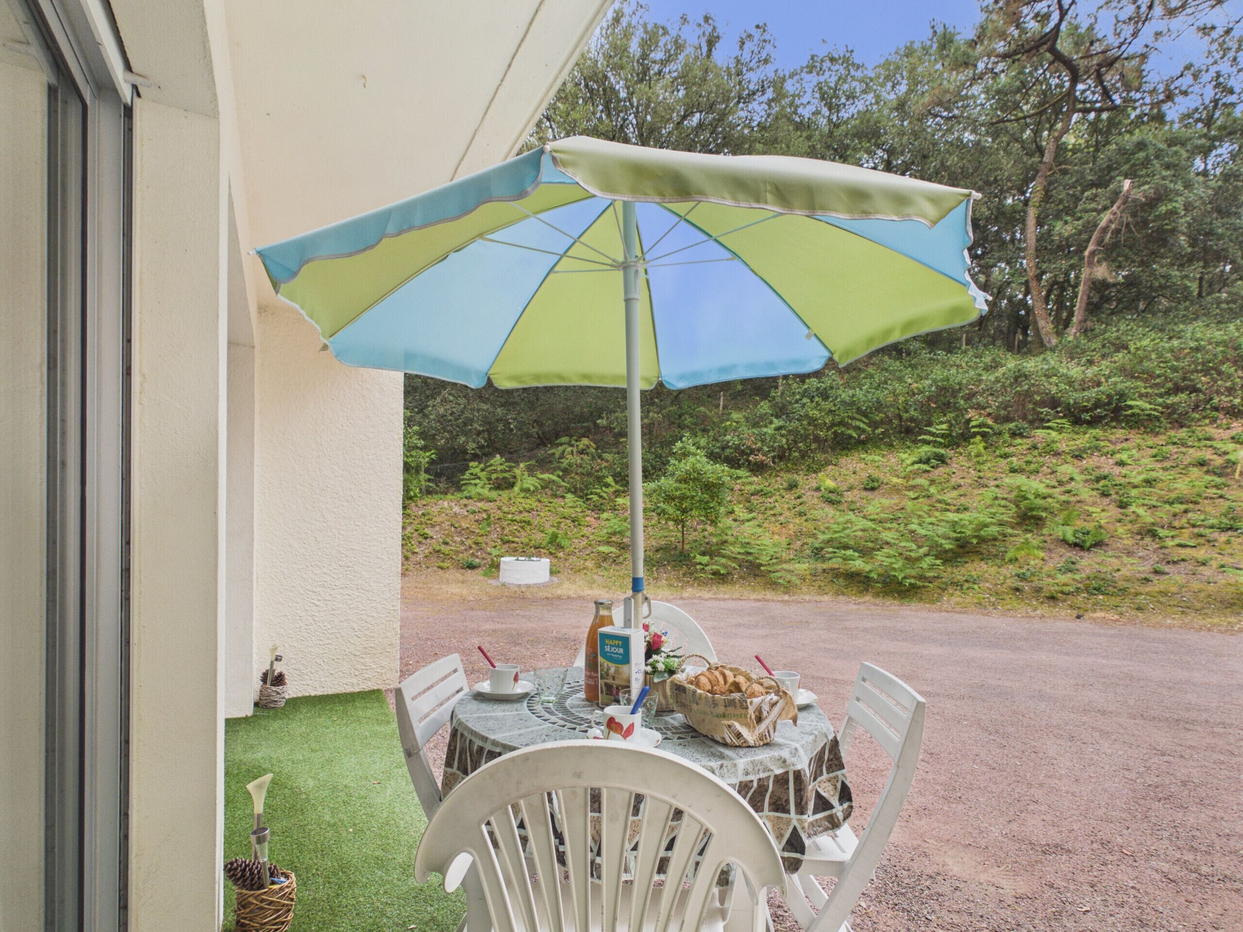 Une terrasse extérieure avec une table, des chaises, un parasol et une bouteille de vin.