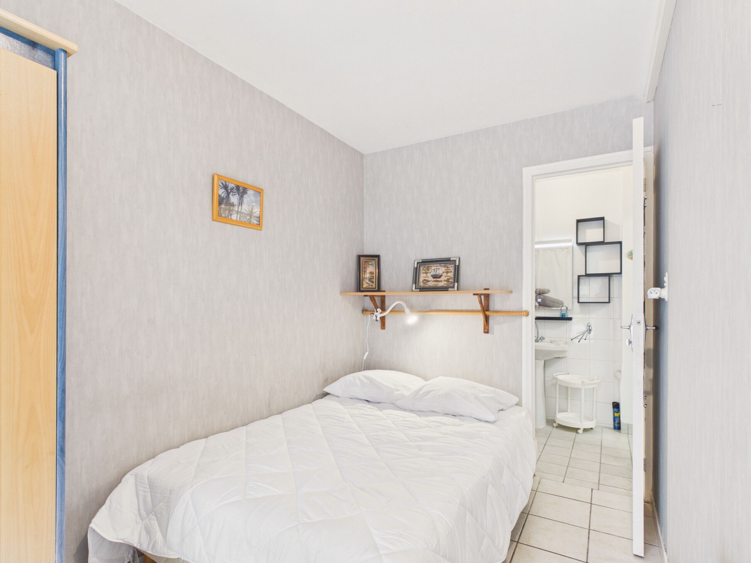 Een slaapkamer met een bed, een houten deur, een wandplank met foto’s, en een badkamer die door een open deur zichtbaar is.