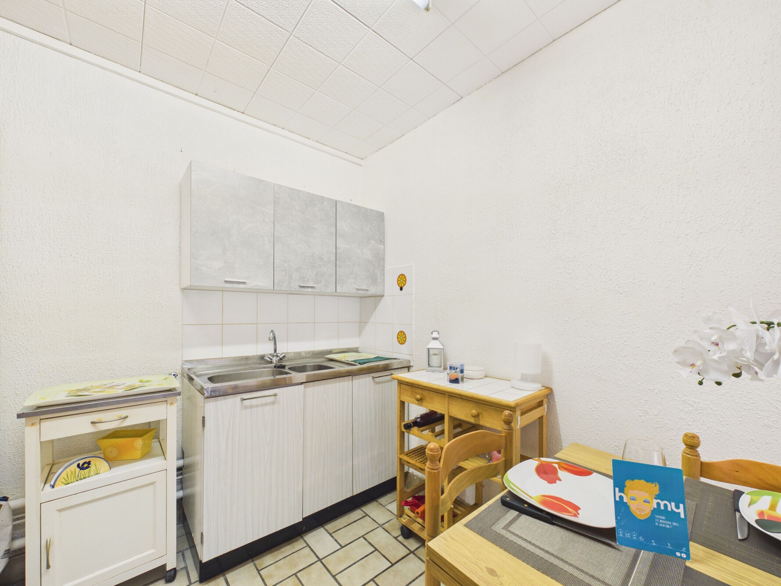 A small kitchenette with a sink, cabinets, a wooden chair, and a table with a placemat.