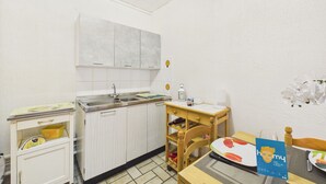 A small kitchenette with a sink, cabinets, a wooden chair, and a table with a placemat. - 700 m from beach , flat for 4 with terrace (Jard-sur-Mer)