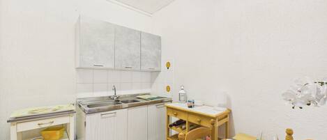 A small kitchenette with a sink, cabinets, a wooden chair, and a table with a placemat.