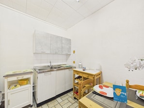 Eine kleine Küchenzeile mit Spüle, Schränken, einem Holzbstuhl und einem Tisch mit Unterlage.