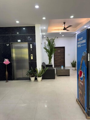 Una hall con una reception, un'ampia pianta in vaso, un distributore d'acqua e una pubblicità di Pepsi.