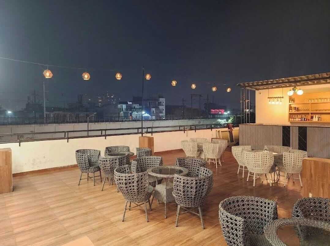 An outdoor seating area with wicker furniture and string lights, overlooking a cityscape at night.