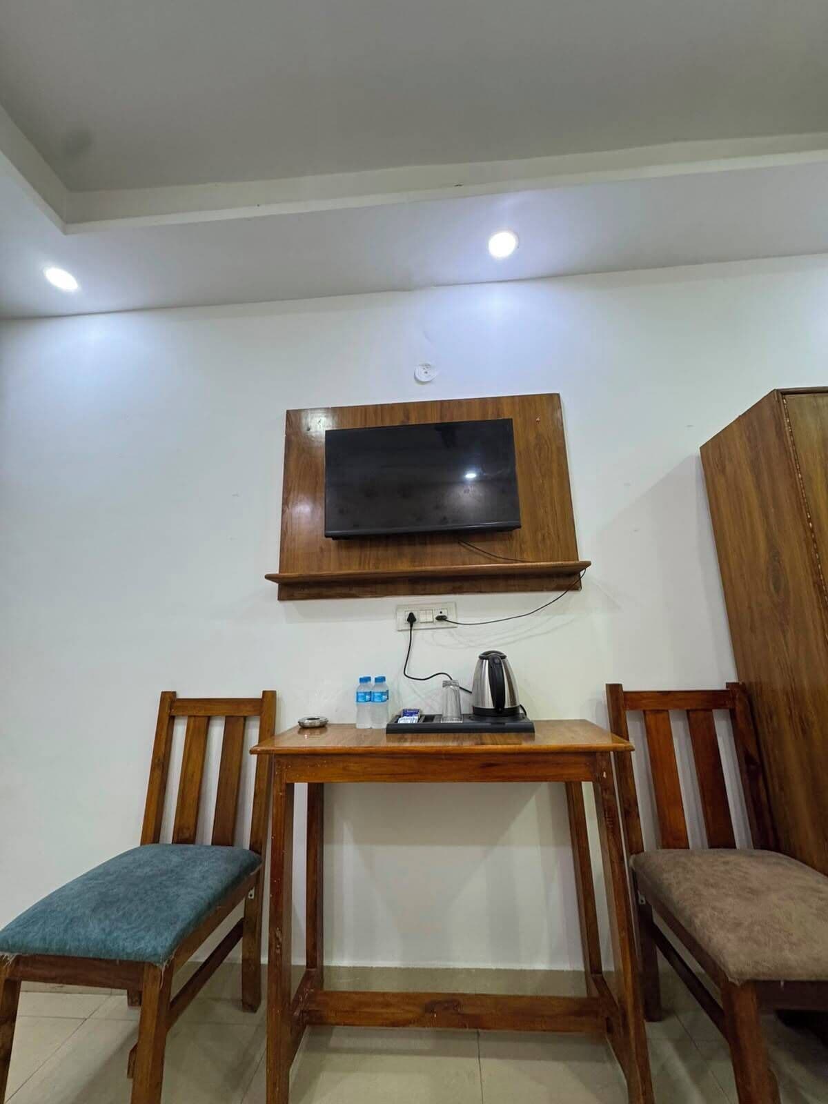 A small room with a TV mounted on the wall, a wooden table with chairs, and a cabinet.
