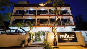 Een meerlaags gebouw met balkons, plantenpotten en een bordje met de tekst 'FROLIC Luxury Stay'.