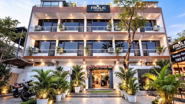 Een meerhoog gebouw met balkons, een bord waarop 'FROLIC LUXURY STAY' staat en bloempotten voor het gebouw.