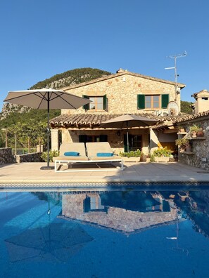 Una villa in pietra con piscina, area relax all'aperto e montagne sullo sfondo.
