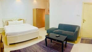 A bedroom with a bed, a sofa, a coffee table, a wardrobe, and a door. - CROWN FURNISHED APARTMENTS SALALAH (SALALAH)
