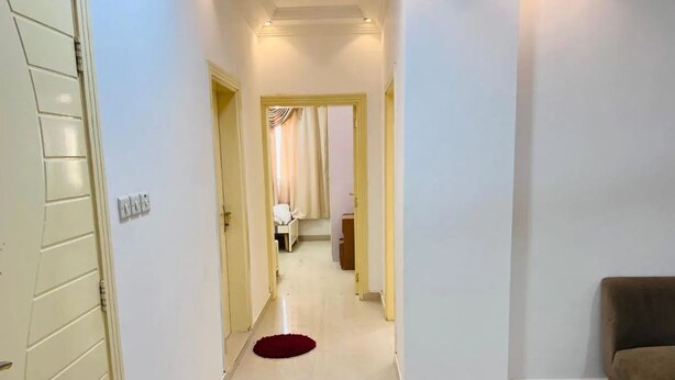 A hallway with a red rug, a couch, and a door on the right. - CROWN FURNISHED APARTMENTS SALALAH (SALALAH)