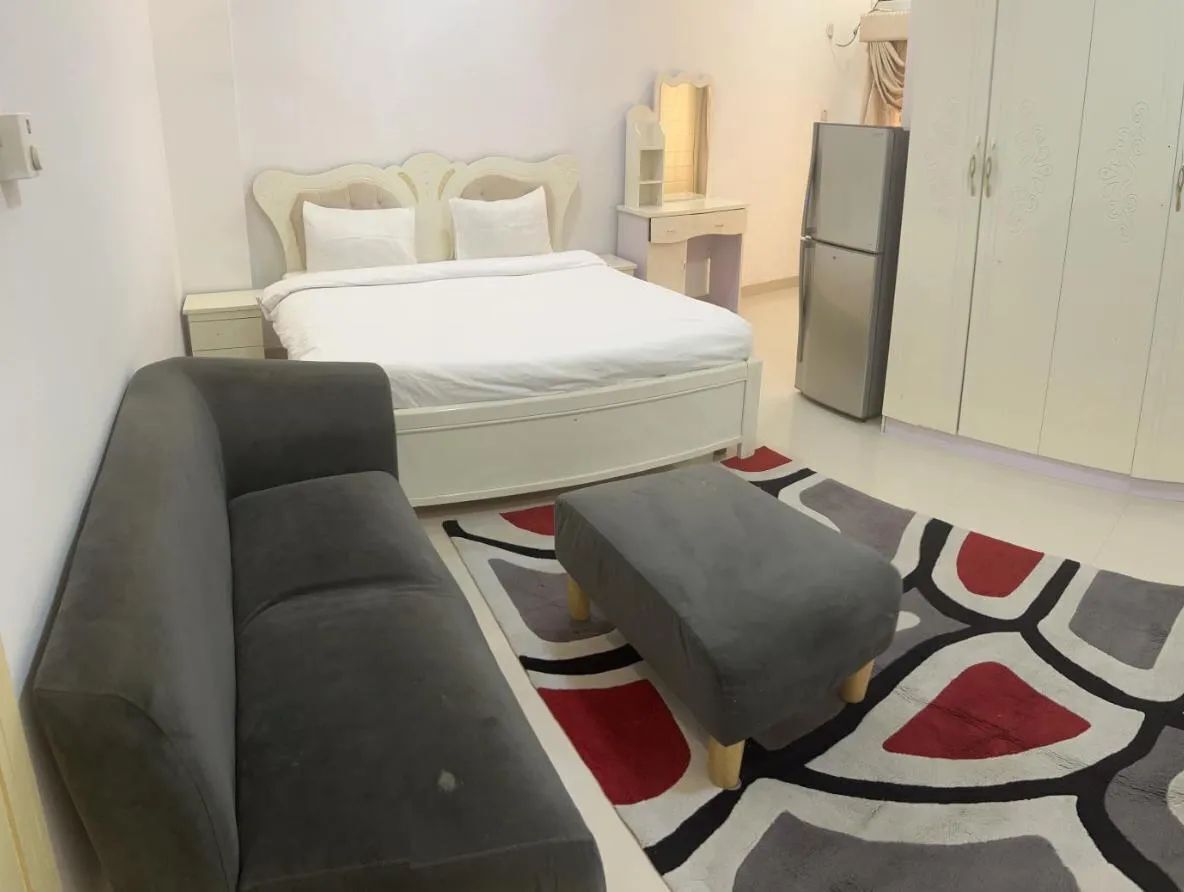 Un dormitorio con una cama, una mesita de noche, un aparador, un refrigerador y un sofá.