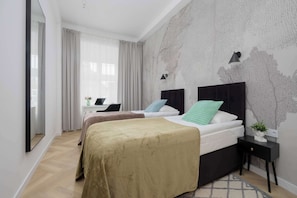 Ein modernes Hotelzimmer mit zwei Betten, einem großen Fenster mit Vorhängen, einer Wand mit einer Baummalerei und einem kleinen Nachttisch mit Pflanze.