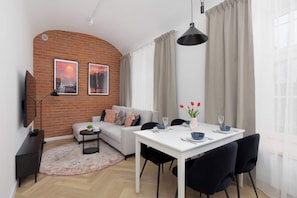 Ein modernes Wohnzimmer mit einer Couch, einem Esstisch und einem an der Wand befestigten Fernseher.