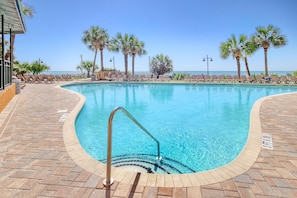 Ein Pool mit klarem, blauem Wasser, umgeben von Liegestühlen und Palmen, mit Blick aufs Meer.