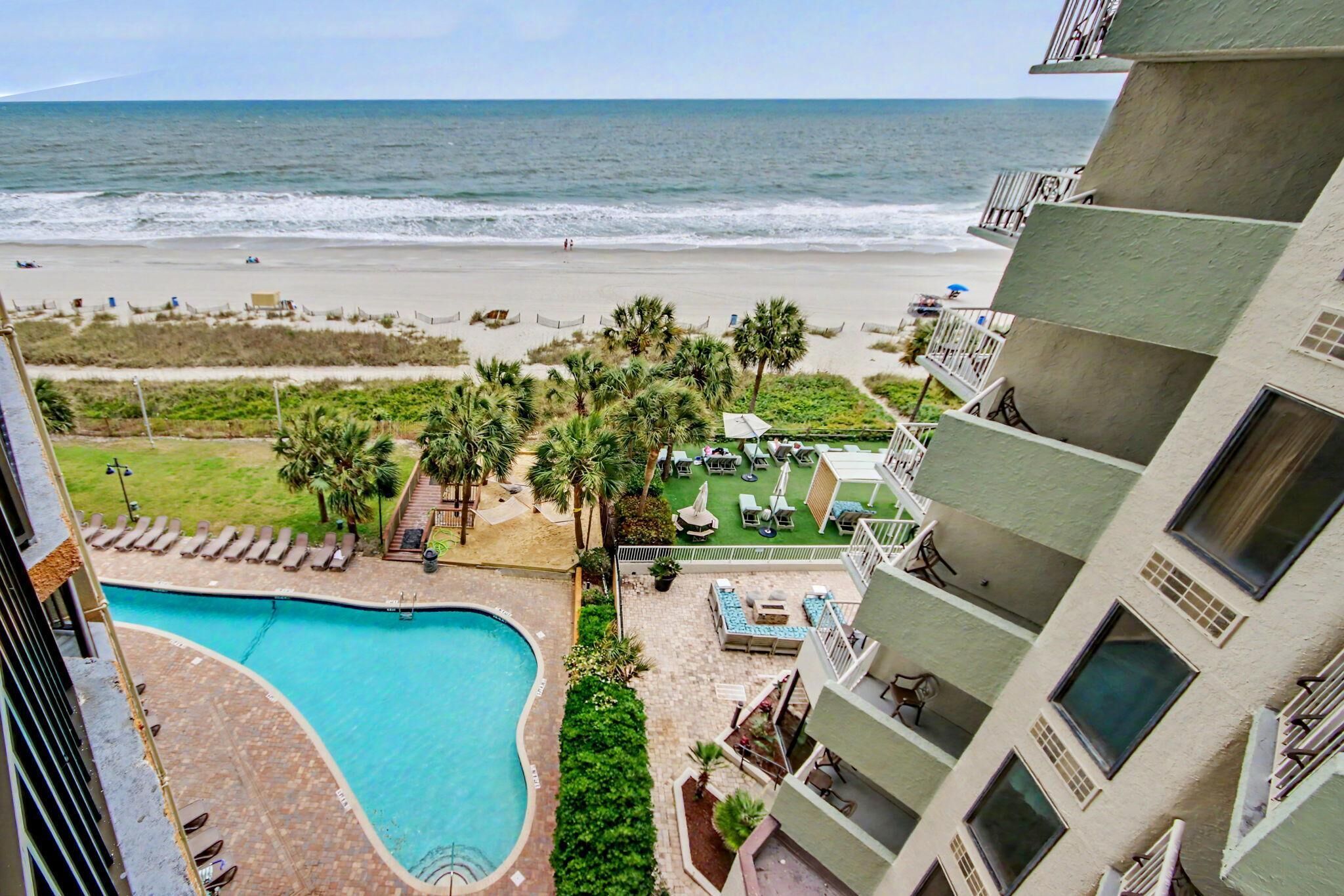 A hotel with a pool, beach view, and outdoor seating area.