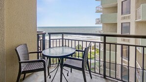Een balkon met een tafel en stoelen, met uitzicht op een strand.