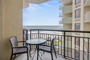 Ein Balkon mit Tisch und Stühlen mit Blick auf einen Strand.