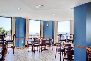 Ein Restaurant mit Holztischen und -stühlen, blauen Wänden und großen Fenstern mit Vorhängen.
