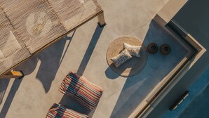 Vista aérea de una terraza en la azotea con piscina, dos sillones reclinables a rayas, una mesa redonda tejida con cojín floral y dos esteras tejidas.
