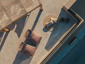 An aerial view of a rooftop terrace with a pool, two striped lounge chairs, a woven round table with a floral cushion, and two woven mats. - Ark Luxury Suite with Hot tub and Sea Views (Zakynthos)