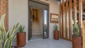 Entrada de un edificio con una escalera que conduce al interior, un letrero que dice 'ARK Luxury Suite' y plantas en macetas.