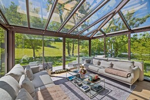 Ein modernes Wohnzimmer mit Glasdach, einer Couch, einem Couchtisch und Blick auf eine grüne Landschaft.
