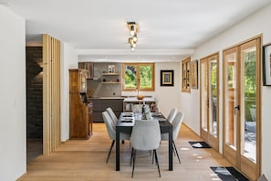 Ein Essbereich mit Tisch für vier Personen, Stühlen, einem Holzschrank und einem Fenster mit Blick auf Grünflächen.