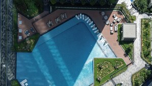 An aerial view of a swimming pool with sun loungers, a small garden, and a paved walkway. - Skyline Views - 39th Floor Apartment (Dubai)