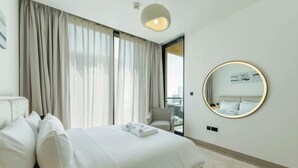 A hotel room with a bed, a chair, a round mirror, and a view of the city. - Skyline Views - 39th Floor Apartment (Dubai)