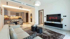 A modern living room with a sofa, a coffee table, a dining area, and a TV displaying 'NETFLIX'. - Skyline Views - 39th Floor Apartment (Dubai)