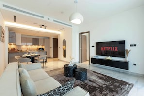 Uma sala de estar moderna com sofá, mesa de centro, área de jantar e TV exibindo 'NETFLIX'.