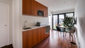 A modern kitchen with wooden cabinets, a built-in microwave, and a sink. There is a dining area with a table and chairs, and a potted plant. - Guestready - Silk Factory Studios and Apartments (Porto)
