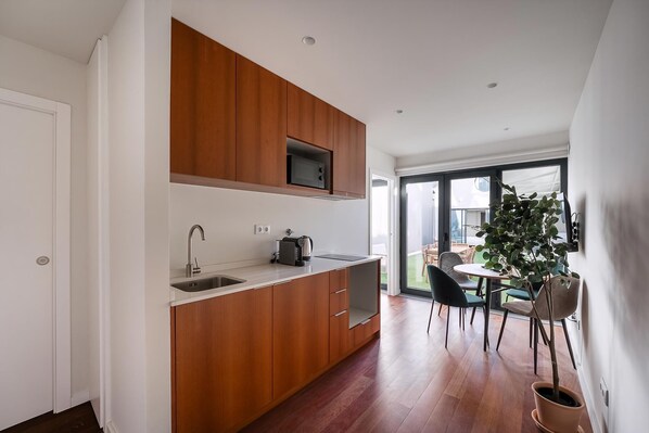 A modern kitchen with wooden cabinets, a built-in microwave, and a sink. There is a dining area with a table and chairs, and a potted plant. - Guestready - Silk Factory Studios and Apartments (Porto)