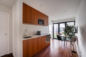 A modern kitchen with wooden cabinets, a built-in microwave, and a sink. There is a dining area with a table and chairs, and a potted plant.