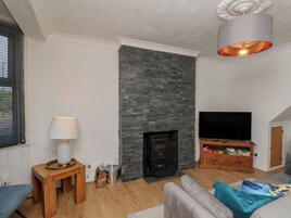 Una sala de estar con chimenea de piedra, un televisor sobre un soporte de madera y una lámpara en una mesita.