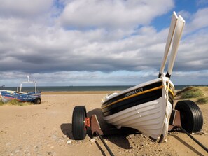 Ein Strand mit einem Ruderboot namens 'MOONRAKER' und einem weiteren Boot im Hintergrund.