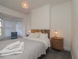 Un dormitorio con cama, mesitas de noche, una silla y una ventana con persianas.