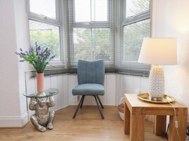 A corner room with a blue chair, a glass table with a monkey sculpture, a lamp, and a window with blinds.